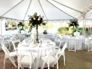 This is a fall lake wedding reception under a tent with bold red florals with the vendors Dorothy McDaniels Florist and Yellow Bicycle Catering at Oak Island Mansion in Wilsonville, Alabama.
